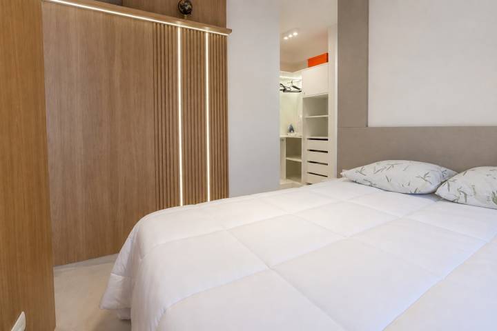 Dormitório com cama de casal, painel amadeirado e acesso ao closet planejado