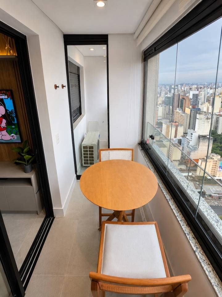 Varanda envidraçada com mesa para duas pessoas e vista urbana do Centro de Campinas