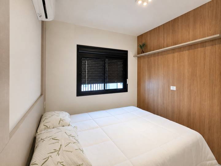 Dormitório climatizado com cama de casal, painel amadeirado e persiana blackout integrada