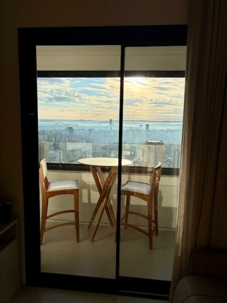 Varanda envidraçada com mesa para duas pessoas e vista panorâmica de Campinas a partir da sala